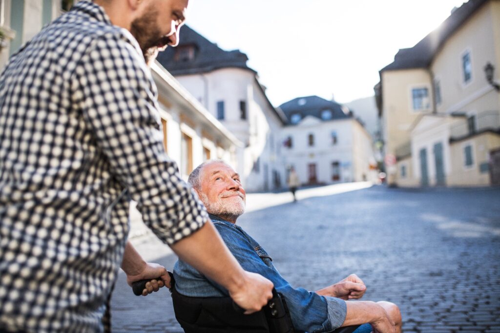 An adult son with senior father in wheelchair on a walk in town.